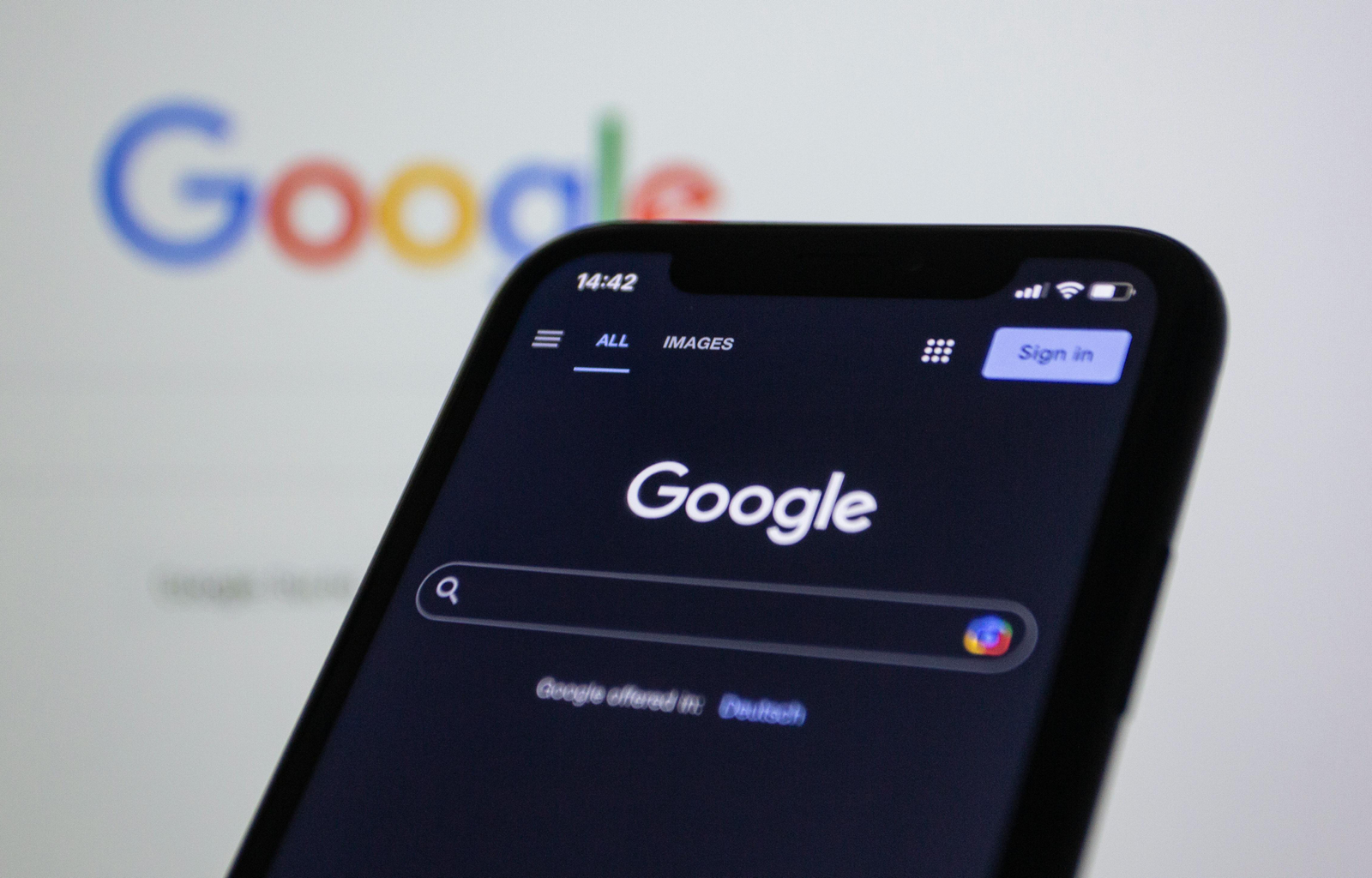 Smartphone screen showing Google search in dark mode with the Google logo in the background.